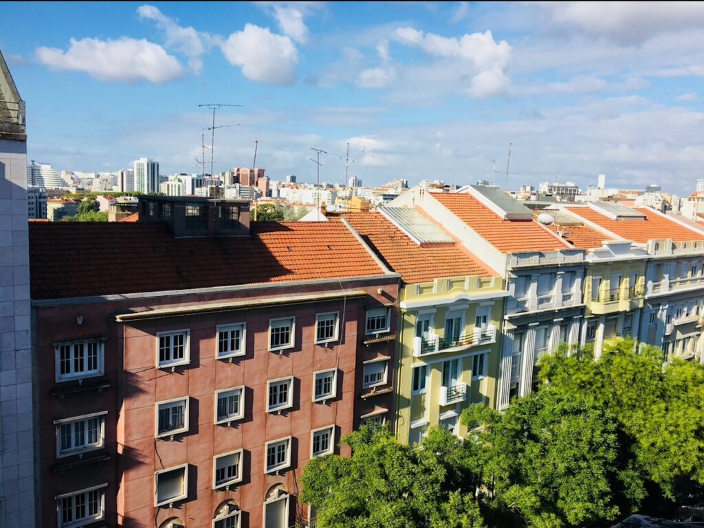View over Lisbon rooftops with tiled buildings, trees, and blue sky