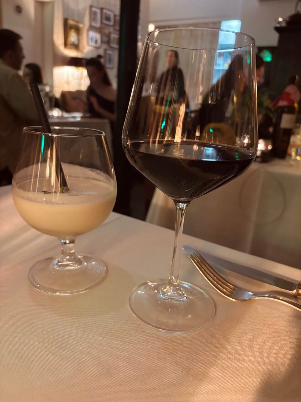 Two glasses of red wine on a wooden table in a dimly lit, cozy bar with warm ambient lights.