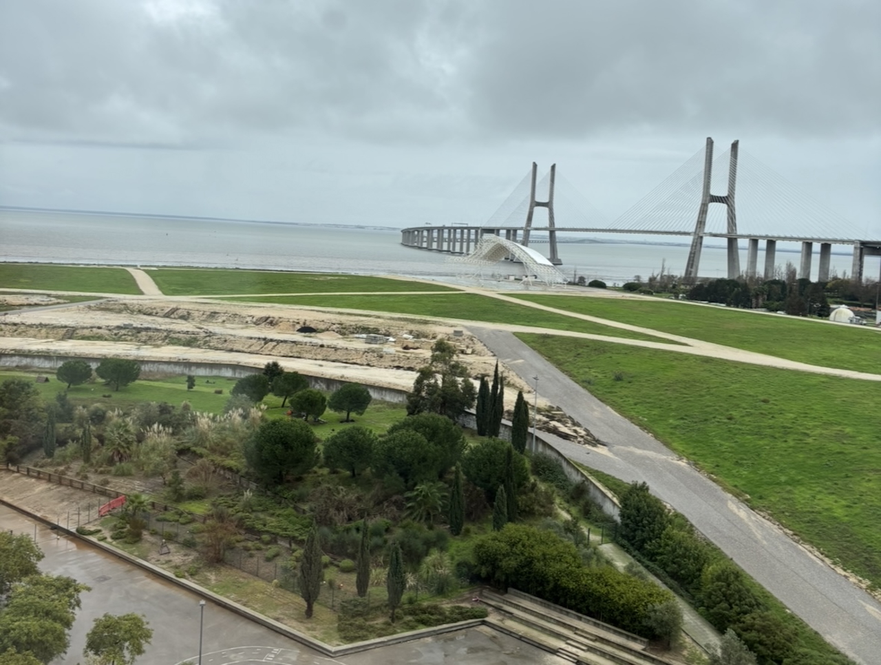 Wide view of the Tagus River, green riverside park, and Vasco da Gama Bridge in Lisbon.