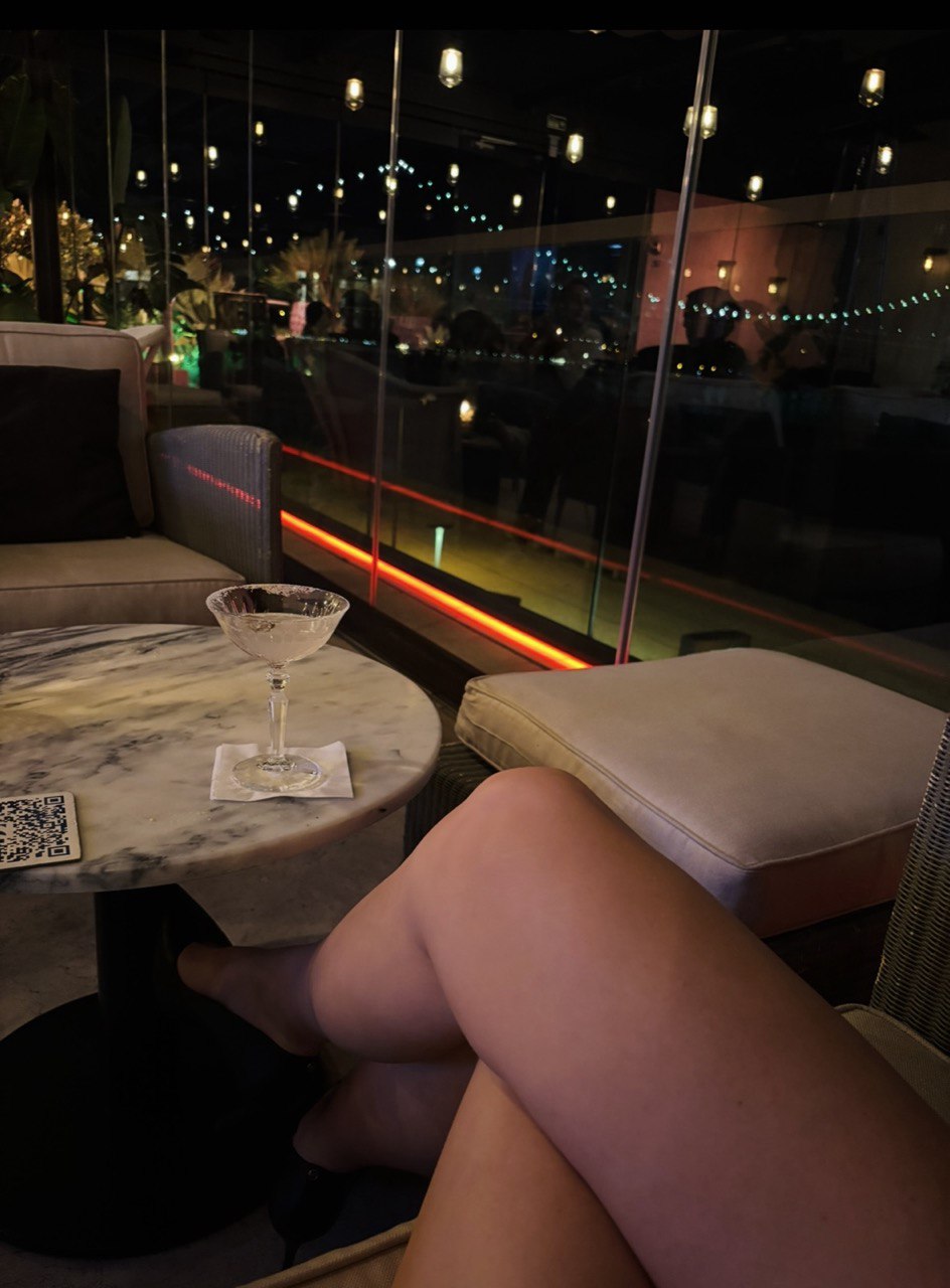 A crushed margarita cocktail and a woman's legs in a dimly lit speakeasy bar in Lisbon, perfect for a mysterious romantic date night.