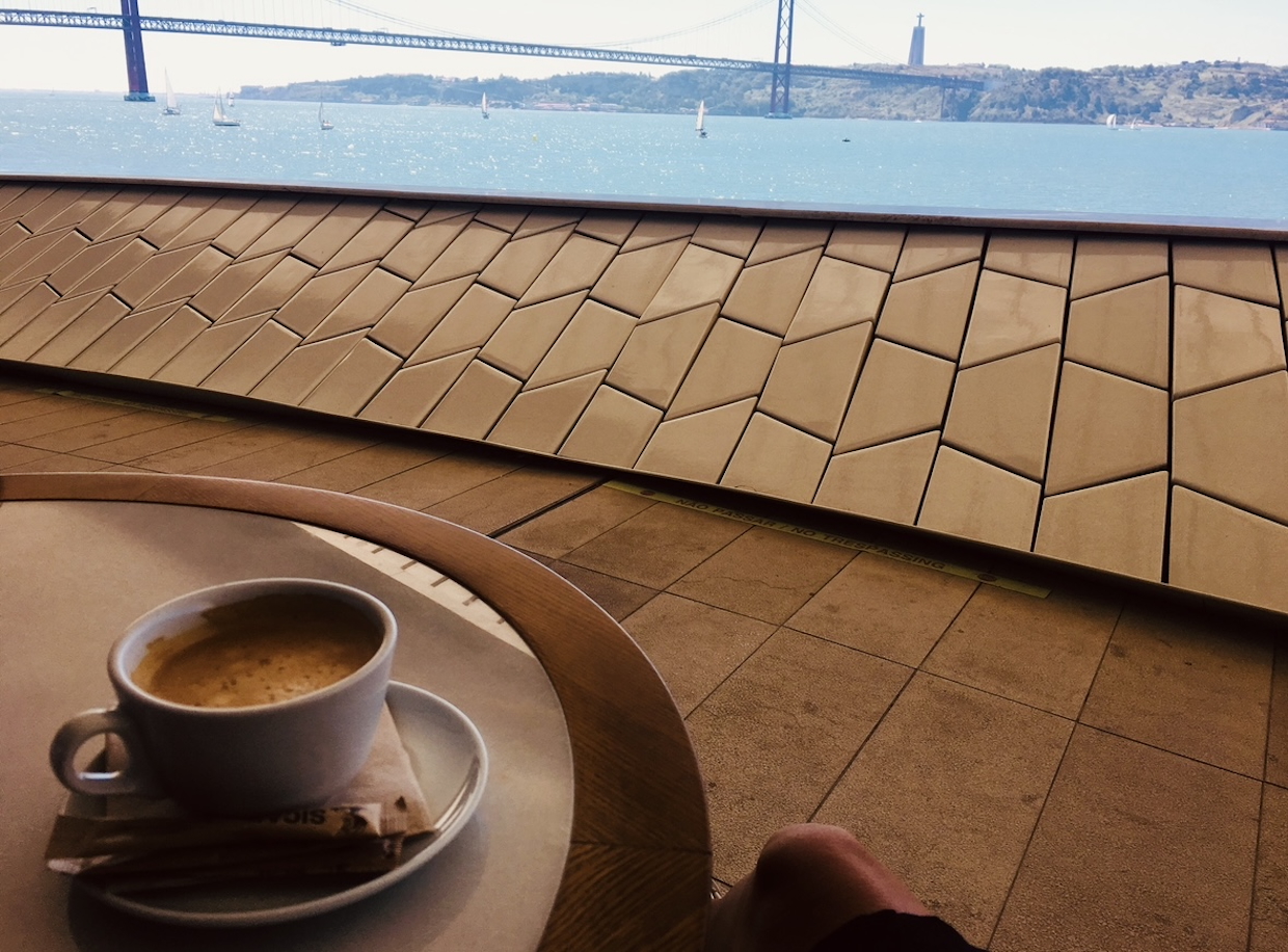 A cup of coffee on a round table at the MAAT Café in Lisbon, offering a scenic view of the Tagus River and the 25 de Abril Bridge. A perfect spot for remote work and inspiration.