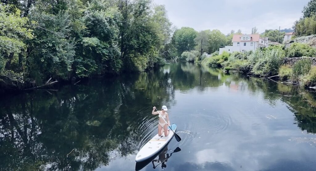 Woman on a stand-up paddle board on a calm river surrounded by trees and houses
